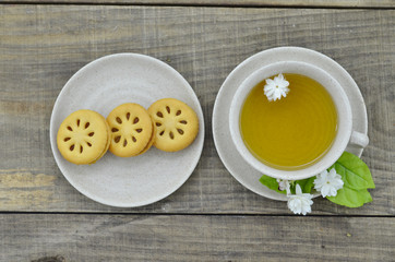 Fresh jasmine tea in cup with cookies on wooden table