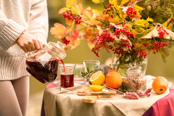 Autumn. A table set on the banks of the lake decorated with a bouquet of autumn leaves. Girl pouring fruit red tea into cups. Tea drinking fruit teas with lemon, apples