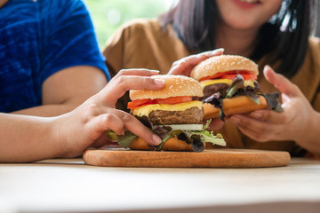Hungry overweight woman smiling and holding hamburger and sitting in the living room, her very...