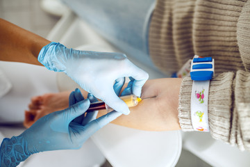Close up of lab assistant with sterile rubber gloves taking blood sample from patient.