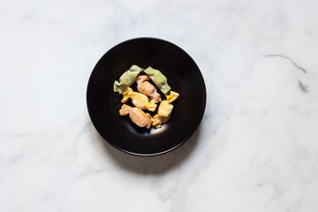 Stuffed Pasta with caramelle shape in a black bowl over a marble counter top view