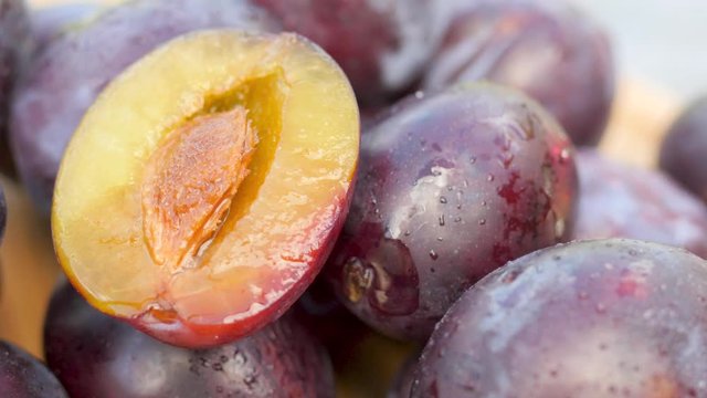 Close-up of fresh juicy wet plums on a wooden table, on top half a plum with a stone. Fruit covered with droplets of water. 360 rotation.