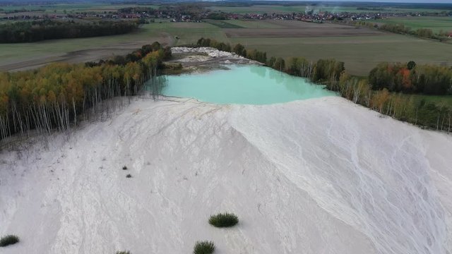 Aerial view of open pit kaolin clay mine (kaolinite quarry) with turquoise pool of water surrounded by autumn landscape with colorful trees - landscape panorama of Poland from above, Europe