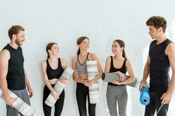 Young people smiling and talking while holding yoga mats