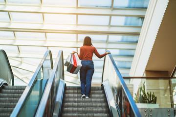 Young woman is walking on the escalator in a mall and shopping