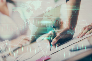 Fototapeta premium A woman hands writing information about stock market in notepad. Forex chart holograms in front. Concept of research. Multi exposure