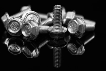 Group of bolts, fasteners close up macro shot on reflecting black surface.