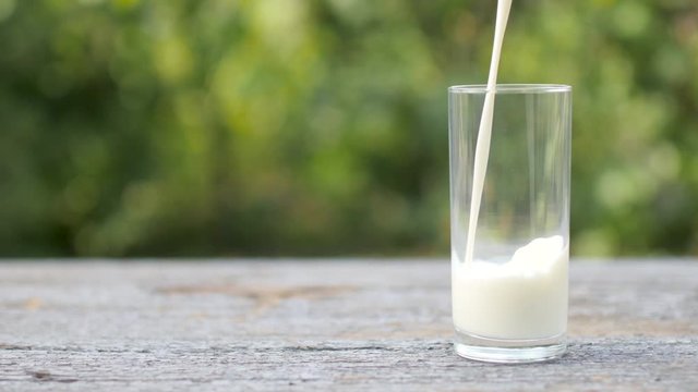 Fresh milk is poured into a glass on a wooden table. Tasty healthy food. A glass of milk. Diet