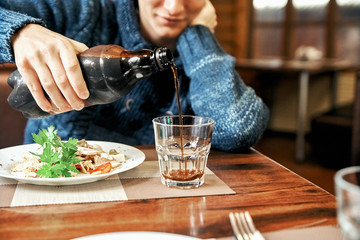 man pours a drink in a glass cup. young guy drinks and eat in a cafe