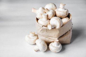 Mushrooms champignons in paper bag on a white wooden table. Place for text or advertising