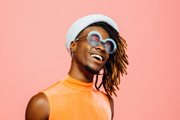 Portrait of a happy young man with sunglasses and cap laughing, isolated on pink