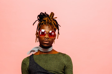 Portrait of a serious young man in green with dreadlocks and red sunglasses, isolated on pink