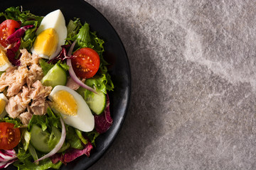 Salad with tuna, egg and vegetables on black plate and gray background. Top view. Copy space