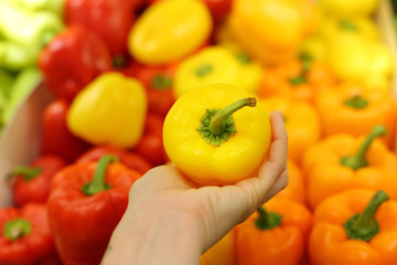 Pepper in hand on a background of a vegetable shelf