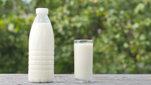 Male hand puts a glass of fresh milk on a wooden table, next to it is a bottle of milk. Organic products. Natural green background. Healthy food concept.