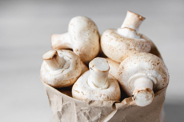 Mushrooms champignons in paper bag on a white wooden table. Close up. Place for text or advertising