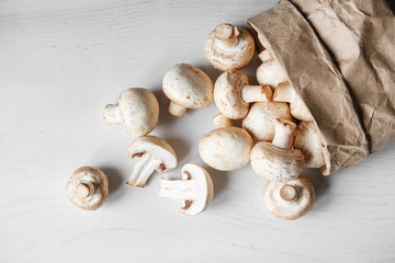 Mushrooms champignons in paper bag on a white wooden table. Place for text or advertising. Top view