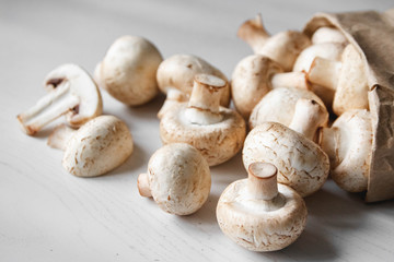 Mushrooms champignons in paper bag on a white wooden table. Place for text or advertising. Top view