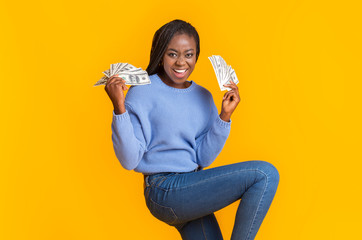Extremely happy young black woman holding money in both hands