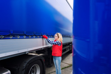 Female truck driver checking vehicle and tightening truck tarpaulin. Transportation services.