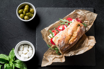 Sandwich with jamon, cheese, tomatoes and arugula on a black background