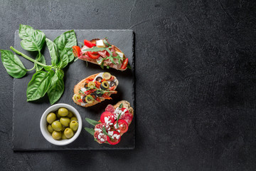 Traditional Bruschetta. Italian antipasti set with jamon, guanchial sausage, olives, cottage cheese, arugula and tomatoes on a black background