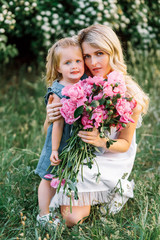 Mom with cute little daughter with flowers outside at the sunset. Concept of happy motherhood
