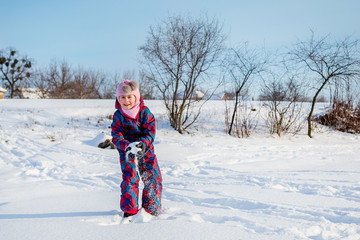 Fototapeta na wymiar Cheerful girl throws snow on a sunny winter day. Active games with snow. The winter vacation.
