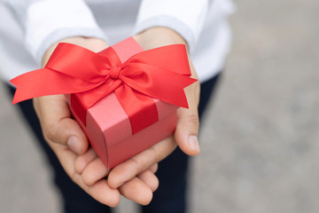 female hands holding gift box red wrapped pack with beautiful ribbon. outdoor background. for surprise special event with copy space. Christmas, birthday or new year concept. High resolution product.