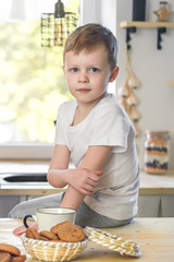 Cute little boy portrait in a white t-shirt sitting on wooden table. Vitamine breakfast in bright kitchen room interior.