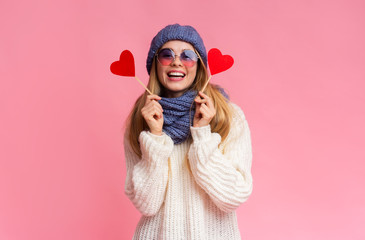 Smiling pretty winter girl in sunglasses with red heart cards
