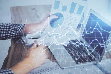 Double exposure of businessman's hands with laptop and stock market graph background. Concept of research and trading.