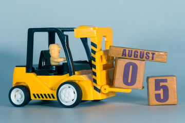 august 5th. Day 5 of month, Construction or warehouse calendar. Yellow toy forklift load wood cubes with date. Work planning and time management. summer month, day of the year concept