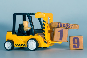 august 19th. Day 19 of month, Construction or warehouse calendar. Yellow toy forklift load wood cubes with date. Work planning and time management. summer month, day of the year concept