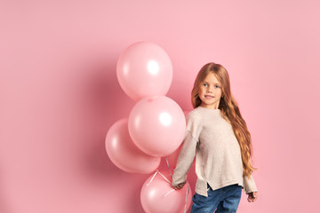 Portrait of funny caucasian kid girl with pink air balloons, long hair and big beautiful eyes, wearing white blouse and jeans.