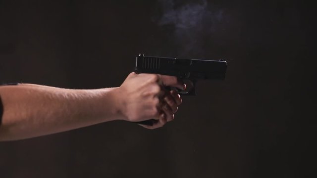 Woman shooting a handgun with recoil.  gun in slow motion. The flame comes out of the mouth of the gun. Indoor black background
