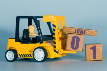 june 1st. Day 1 of month,  Construction or warehouse calendar. Yellow toy forklift load wood cubes with date. Work planning and time management. summer month, day of the year concept