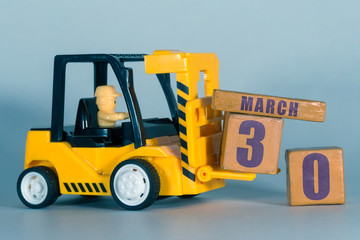 march 30th. Day 30 of month, Construction or warehouse calendar. Yellow toy forklift load wood cubes with date. Work planning and time management. spring month, day of the year concept