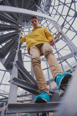 A young guy in a yellow hoodie and turquoise sneakers stands on a spiral staircase. Teen jumps off with a beautiful spiral staircase in the beautiful architecture