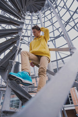 A young guy in a yellow hoodie and turquoise sneakers stands on a spiral staircase. Teen jumps off with a beautiful spiral staircase in the beautiful architecture