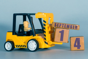 september 14th. Day 14 of month, Construction or warehouse calendar. Yellow toy forklift load wood cubes with date. Work planning and time management. autumn month, day of the year concept