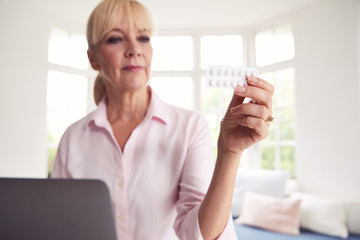 Mature Woman At Home Looking Up Information About Medication Online Using Laptop