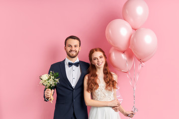Handsome man in tuxedo and redhaired woman in wedding dress look at each other with love. Holding...