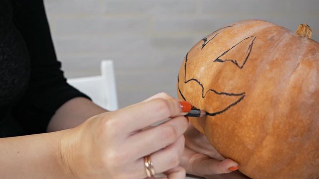 Drawing a funny face on a pumpkin with a black marker.draw halloween pumpkin ready to carving
