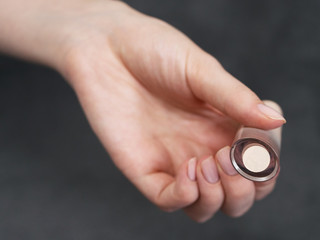 Fototapeta premium Woman's beauty blogger hands holding professional hi-end lipstick cosmetics with blurred grey background, applies sample tone color on skin with copyspace