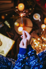  The atmosphere of the New Year or Christmas, a girl in blue festive pajamas holds a burning sparkler in her hands