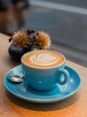 One cup of cappuccino with latte art on wooden table, blue ceramic cup, top view. Cafe culture.