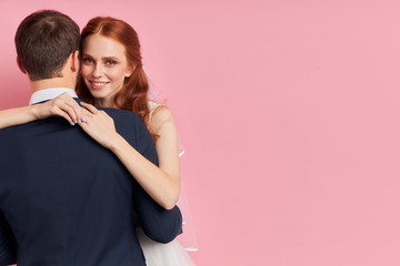 Rear view on man in tux with hugging him smiling woman, isolated over pink background. Love