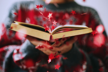  New Year and Christmas, girl blows shiny red stars out of the book in her hands 