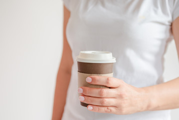 Woman in a white t-shirt holds morning coffee in a paper cup